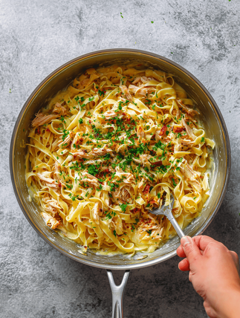 Fettuccine and chicken being mixed with Alfredo sauce in a bowl
